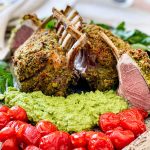 Close up of the cooked lamb racks with pea puree and blistered tomatoes. One of the racks has been cut into showing the beautiful pink lamb meat inside.