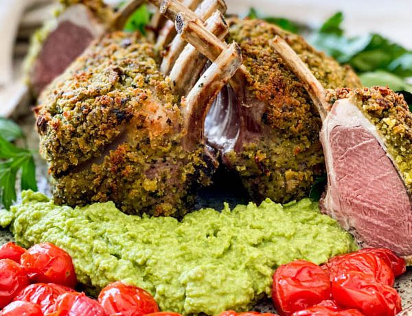 Close up of the cooked lamb racks with pea puree and blistered tomatoes. One of the racks has been cut into showing the beautiful pink lamb meat inside.