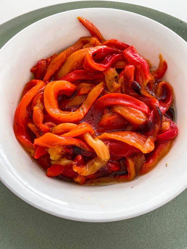 Roasted red capsicum slices in a bowl with olive oil drizzled over.