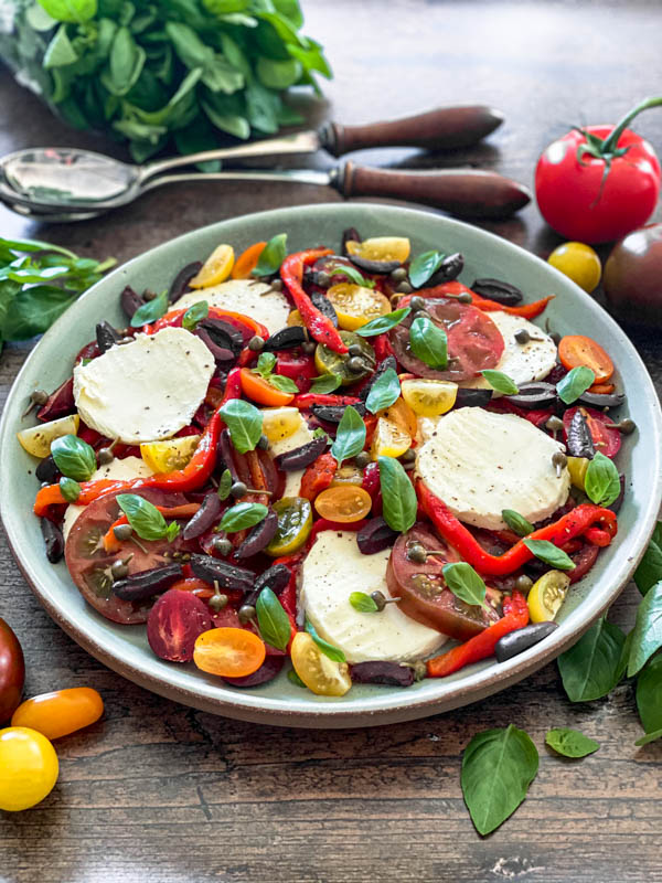 A platter of Caprese Salad with basil leaves and tomatoes surrounding it.