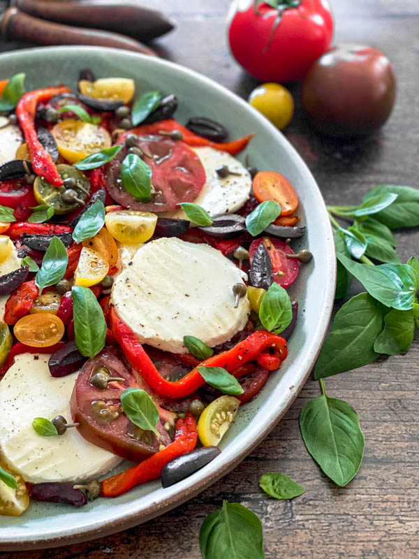 This shows half the platter of Caprese Salad with basil leaves around it.