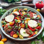 The Caprese Salad on a green platter with serving spoons behind it.