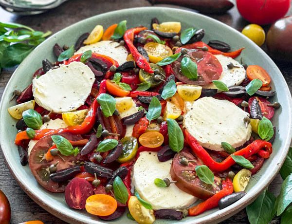 The Caprese Salad on a green platter with serving spoons behind it.