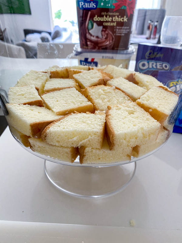 A layer of cubed sponge is placed in the bottom of a trifle bowl.