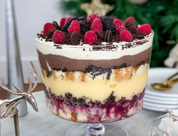 The finished trifle is on the table with plates and spoons in the background.