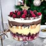 The trifle is in a trifle bowl with a pedestal base and is on a marble table ready to be eaten.