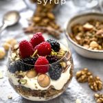 The glass of granola, yoghurt and fresh berries in the foreground, with a bowl of granola and spoons in the background.