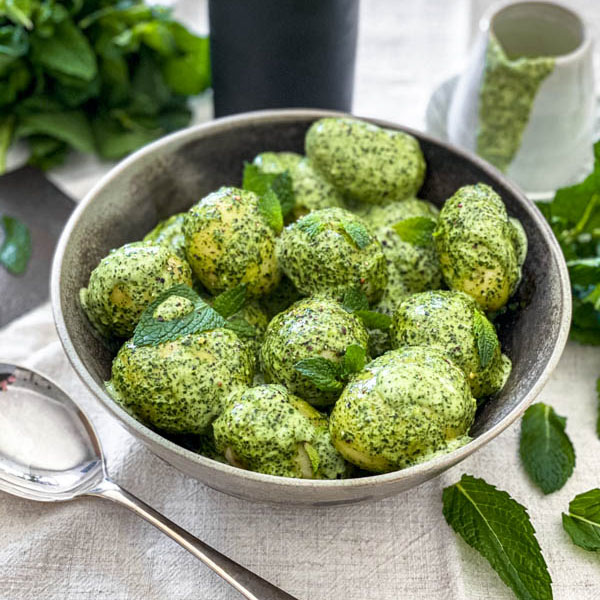 The New Potato Salad with Mint Dressing is in a bowl on a table with a jug of the Mint Dressing in the background.