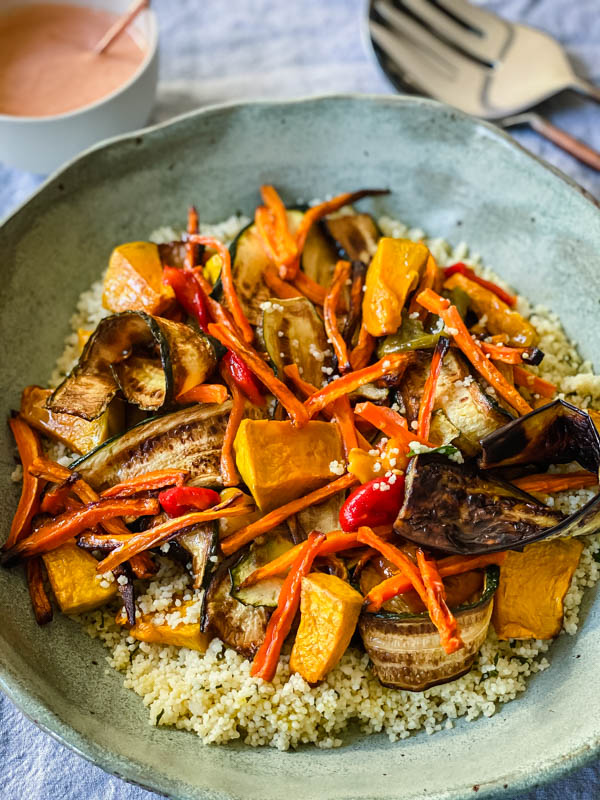 The bowl of Grilled Vegetable and Couscous Salad is in a bowl on a table with the Red Pepper Mayo and salad servers in the background.