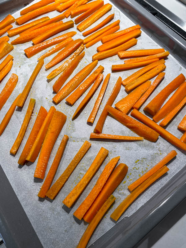 Carrot sticks on an oven tray lined with baking paper ready to be cooked in the oven.