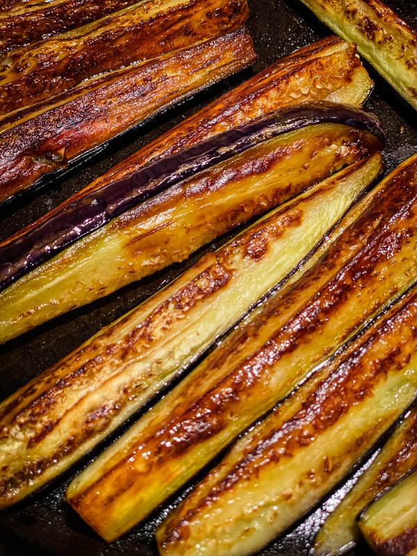 Quartered baby eggplant charred and browned, cooking on a bbq plate.