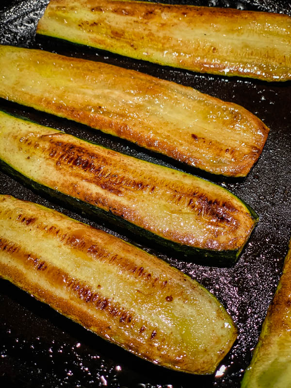 Charred and browned zucchini slices are cooking on a bbq plate.