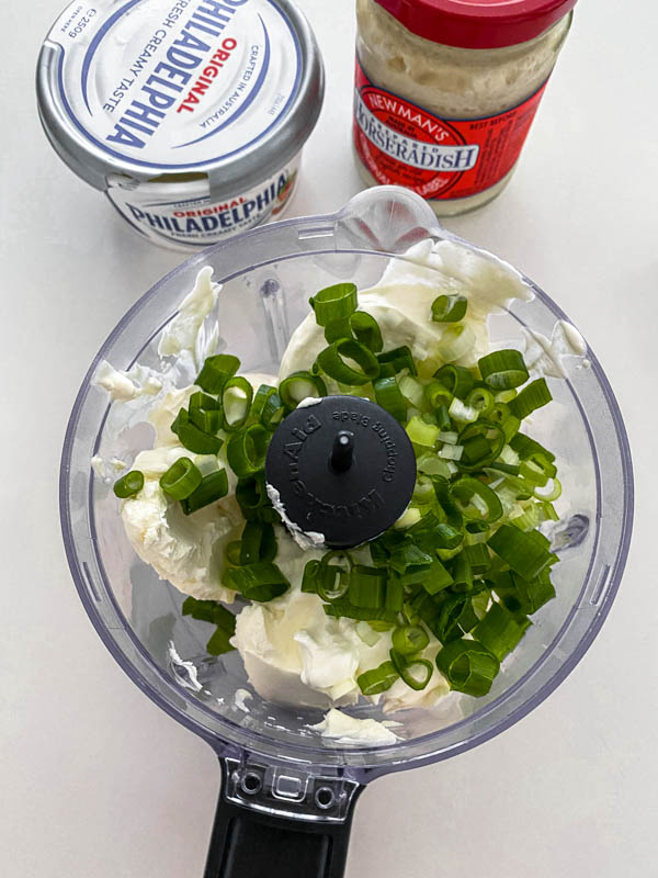 The first of the ingredients, the cream cheese, horseradish and spring onions are added to the bowl of a mini food processor.