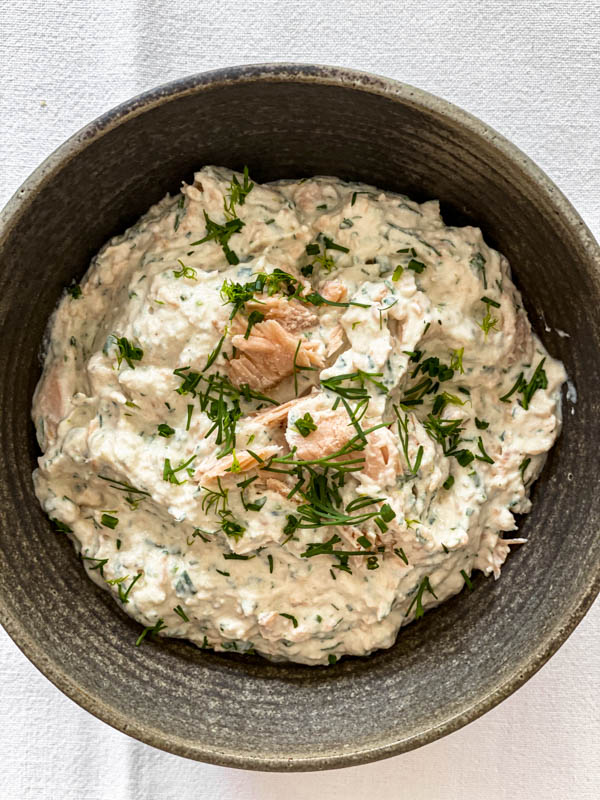 The Smoked Salmon Dip is in a bowl ready to be served. It is garnished with extra herbs and some flaked smoked salmon on top.