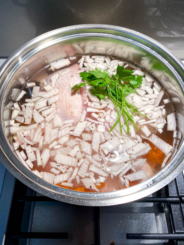 The bone-in chicken pieces are in a pot of water with onions, carrots and parsley stalks ready to be boiled to make stock for the soup.