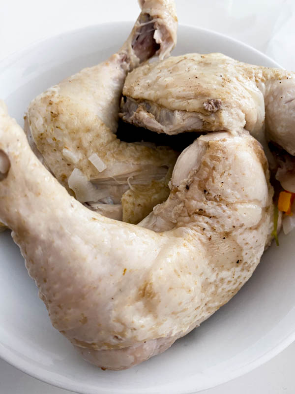 The chicken pieces have been cooked and are now resting in a bowl to cool down, before the meat is removed from the bones and added back into the soup.