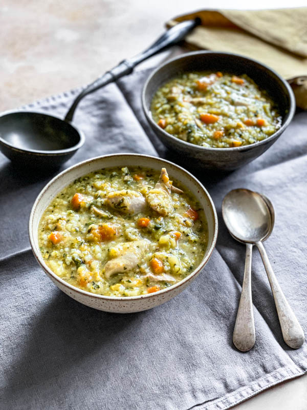 Two bowls of soup are sitting on a placemat with soup spoons and a ladle beside them.