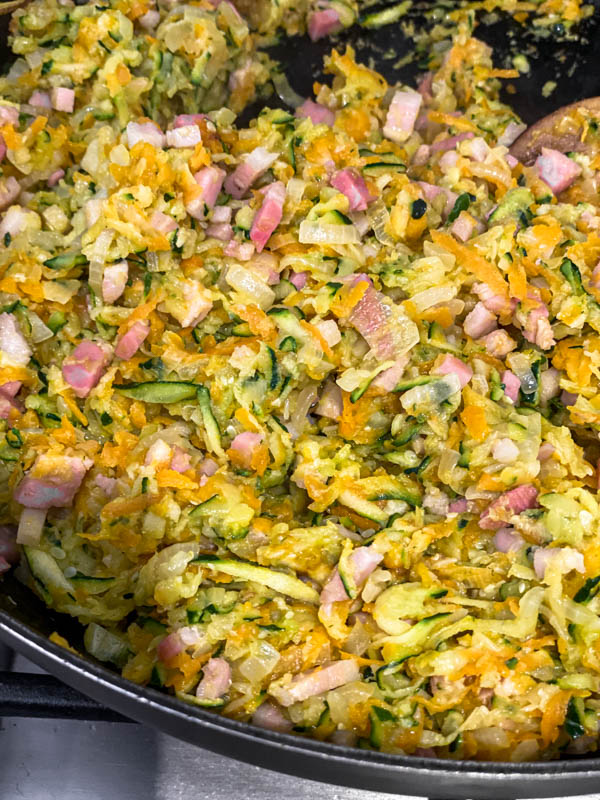 A close up showing the sautéed onions, carrot, zucchini, garlic and bacon that is now ready for the eggs and flour to be added.