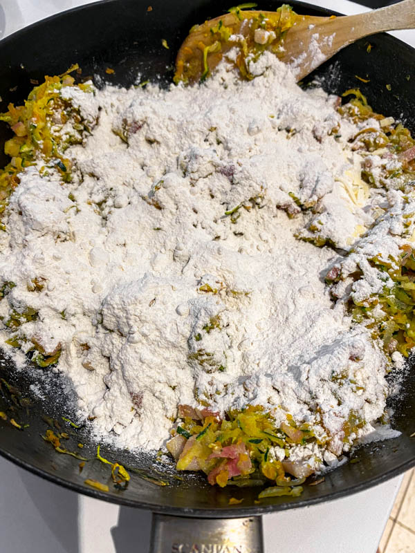The flour and cheese are added to the sautéed vegetables in the frying pan.