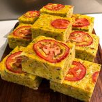 A close up of the portioned squares of zucchini slice presented on a wooden chopping board.