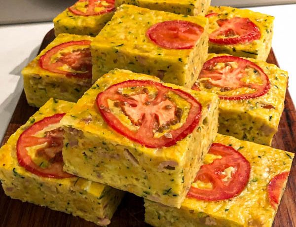 A close up of the portioned squares of zucchini slice presented on a wooden chopping board.