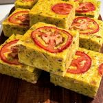 The zucchini slice is cut into squares and sitting on a wooden chopping board.