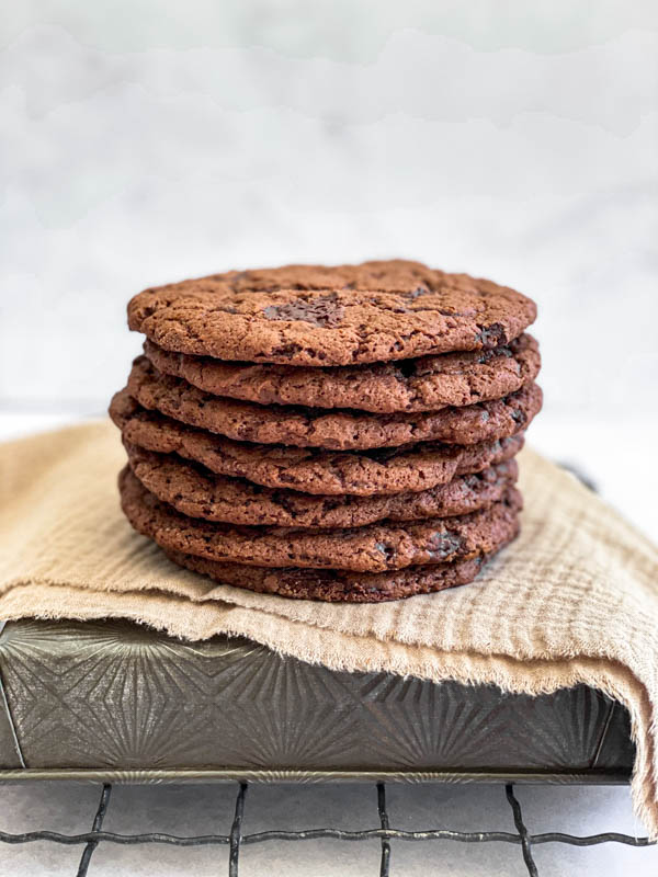 A pile of seven cookies on top of each other are sitting on top of an overturned baking tray with a linen cloth draped over it.