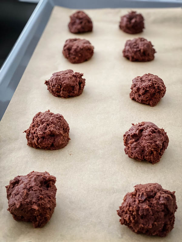 Spoonfuls of uncooked cookie dough sitting on a baking tray lined with baking paper ready to be put in the oven.