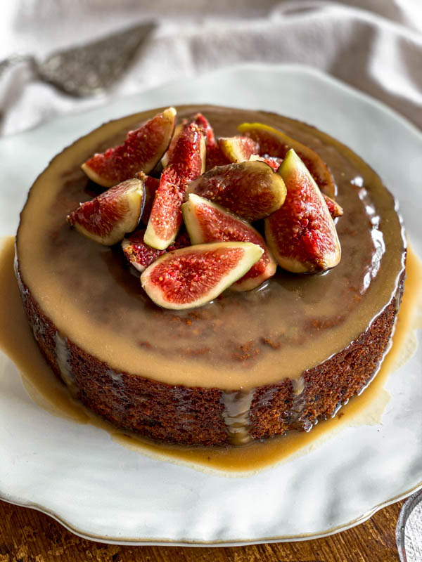 The Sticky Date Pudding is on a plate with the caramel sauce poured over the top. It is decorated with a pile of fresh quartered figs on top.