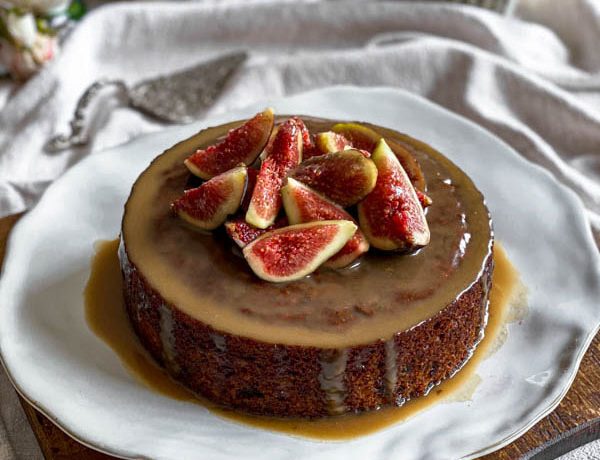 The Sticky Date Pudding is on a plate on top of a wooden board and sitting on a linen tablecloth.