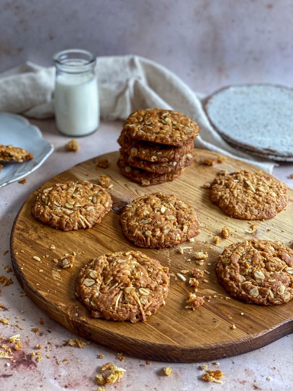 There are a pile of 4 biscuits and some single ones on a round wooden tray with biscuit crumbs around them.