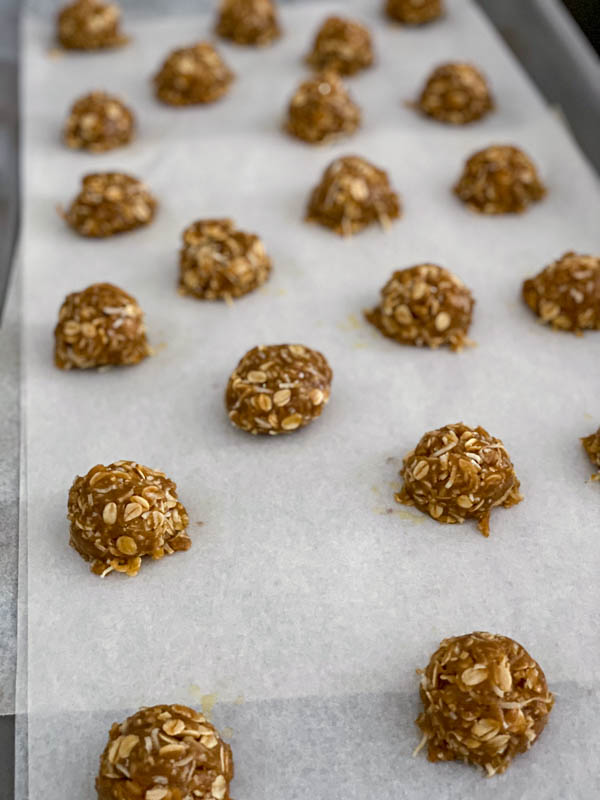 The balls of biscuit dough are on an oven tray lined with baking paper, ready for the oven.