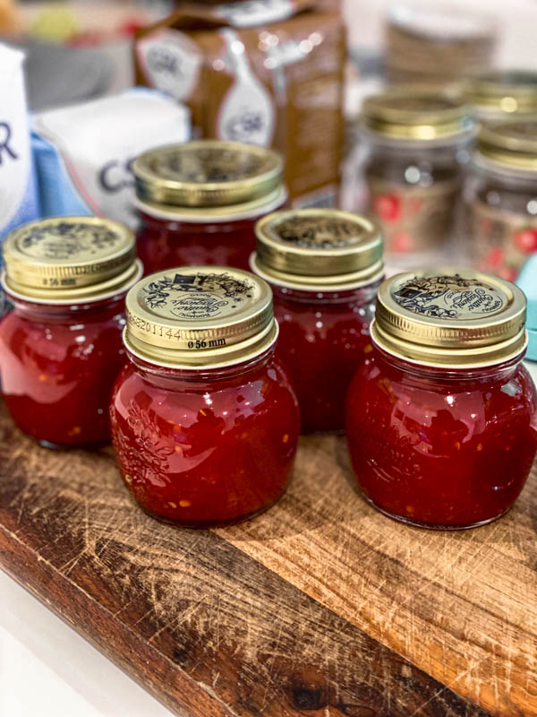 This shows jars of the prepared Tomato Chilli Jam all finished and sitting on a wooden board.