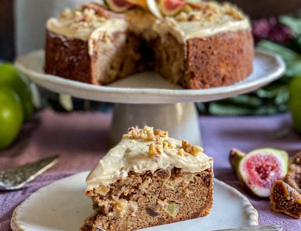 A slice of cake in the foreground with the rest of the cake behind it on a cake stand.