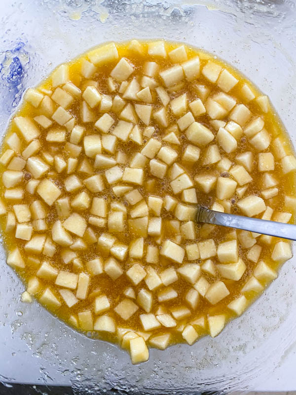 The diced apple is added to the bowl along with the melted butter and sugars.