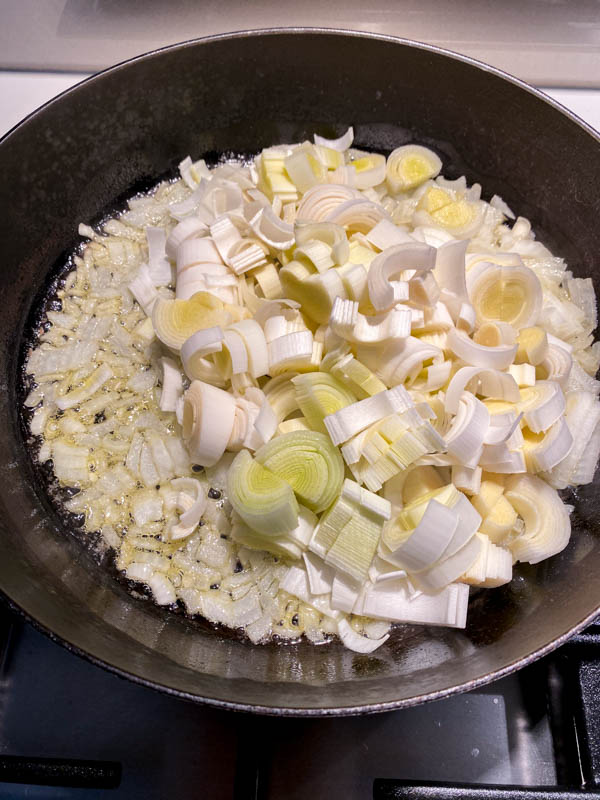 Looking down into the frying pan with the chopped onions cooking inside. The chopped leeks have just been added to the pan.