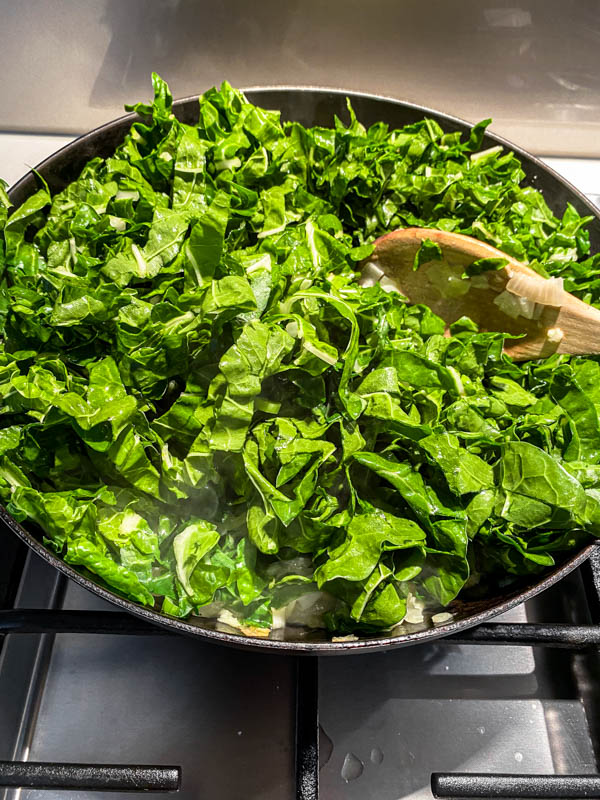 The chopped silverbeet is added to the frying pan.