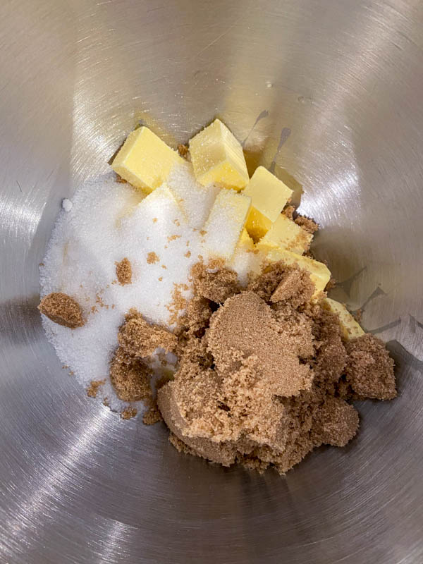 The cold cubed butter and sugars are in the bowl of a stand mixer ready to be beaten together to form a paste.