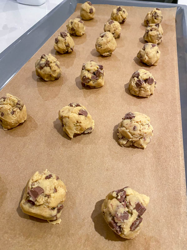 The balls of cookie dough are on an oven tray lined with baking paper. They are shaped into rough balls, not rolled.