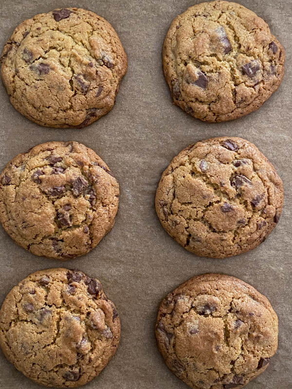 Looking down onto 6 chocolate chip cookies resting on the oven tray.