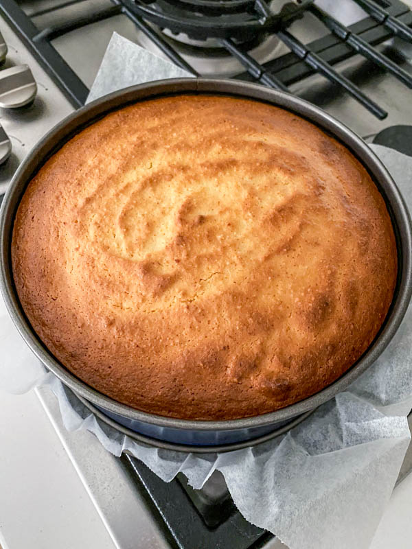 The baked cake is golden brown on top and resting/cooling in the cake tin.