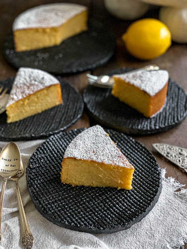 Slices of cake are on black serving plates. The cake is dusted liberally with icing sugar.