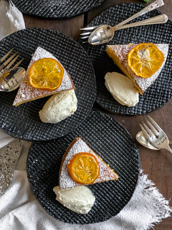 Looking down onto 3 slices of lemon cake. Each slice is topped with a confit lemon slice and has been dusted with icing sugar. They also have a dollop of yoghurt beside each cake slice.