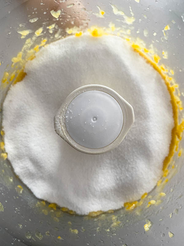 The sugar is placed on top of the lemon puree in the bowl of a food processor.