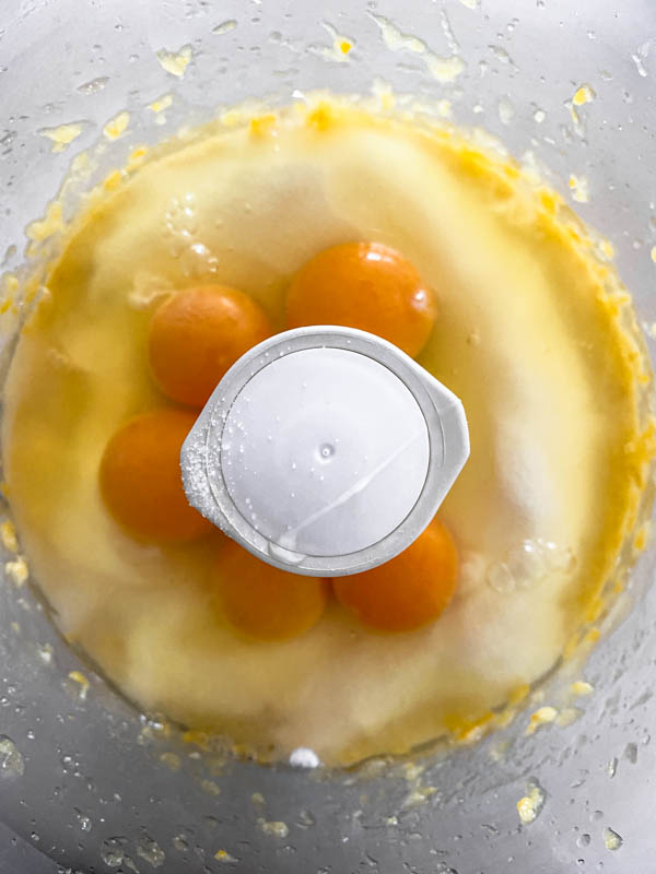 The eggs are placed on top of the sugar in the food processor bowl.