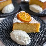 A close up of a slice of the lemon cake on a black textured plate. It is served with a dollop of yoghurt and a slice of confit lemon.