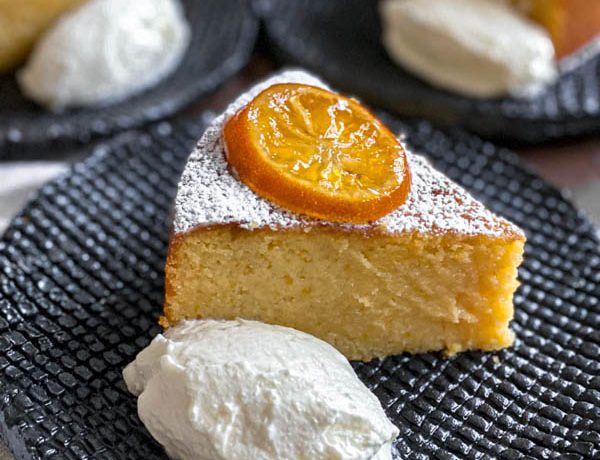 A close up of a slice of the lemon cake on a black textured plate. It is served with a dollop of yoghurt and a slice of confit lemon.