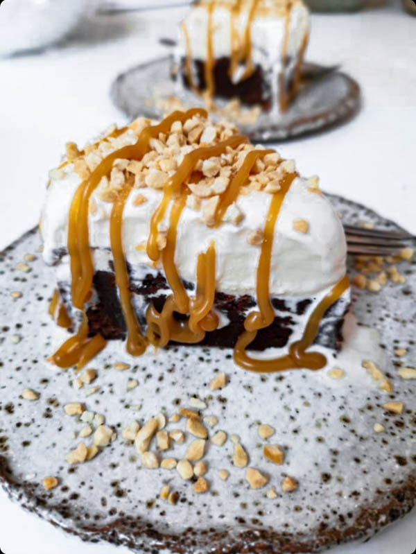 A close-up of a slice of Chocolate Brownie Ice Cream Cake that has been decorated with chopped roasted peanuts and a salted caramel drizzle.