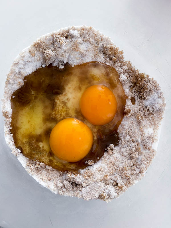 The eggs and sugars are in a glass bowl ready to be beaten together with a hand-held whisk.