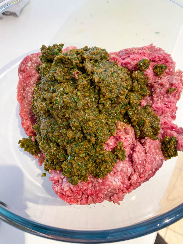 The herb and spice mix is added to the mince meat in a glass bowl.